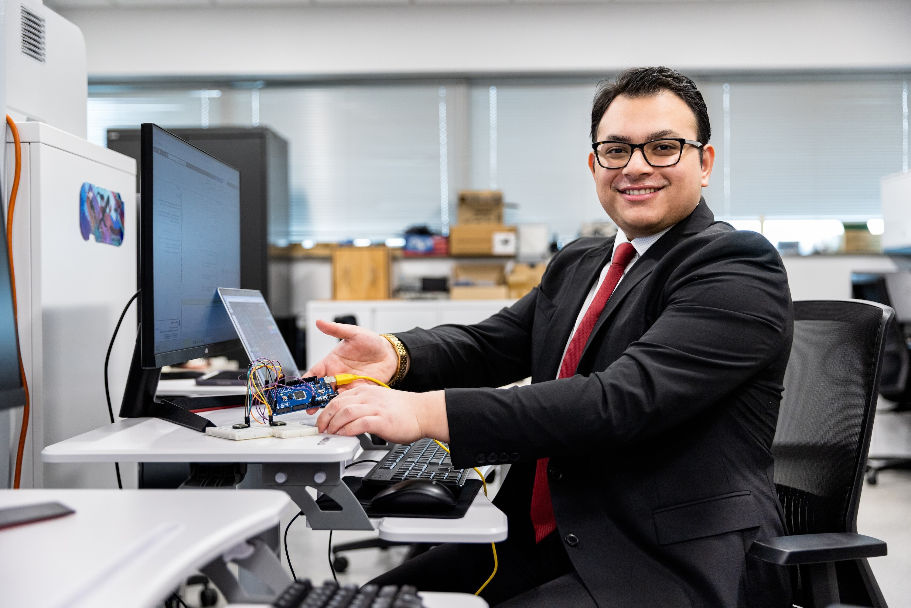 NJIT graduate Krish Poudel '26 sits at a desk, holding up a small electronic device.