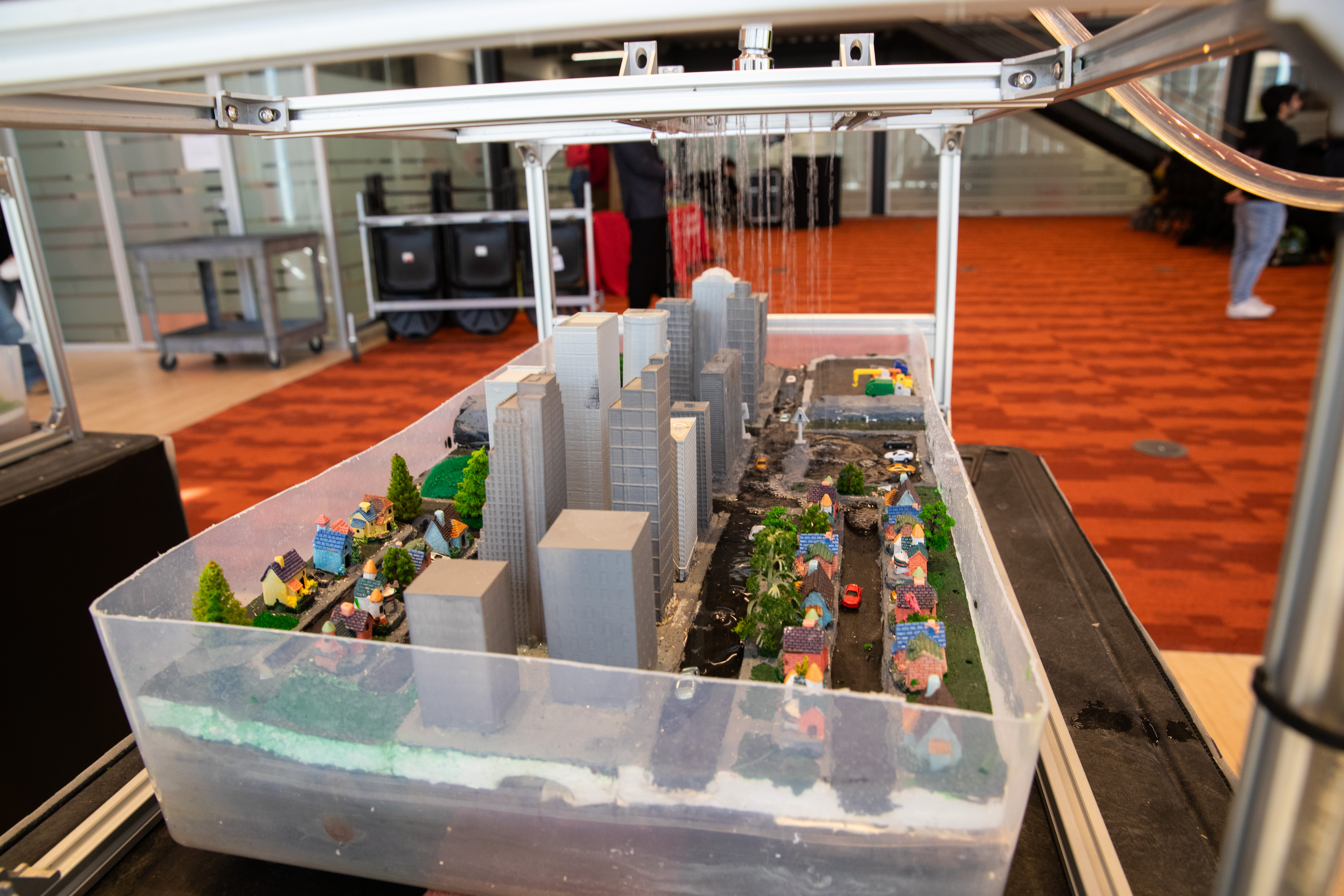 A 3D model of a city in a plastic tub. Overhead, a showerhead simulates rainfall.