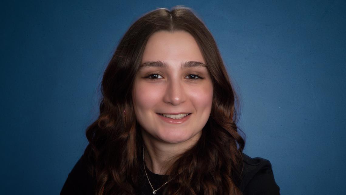 Studio portrait of NJIT graduate Kaily Peixoto '26 against a blue gradient background.