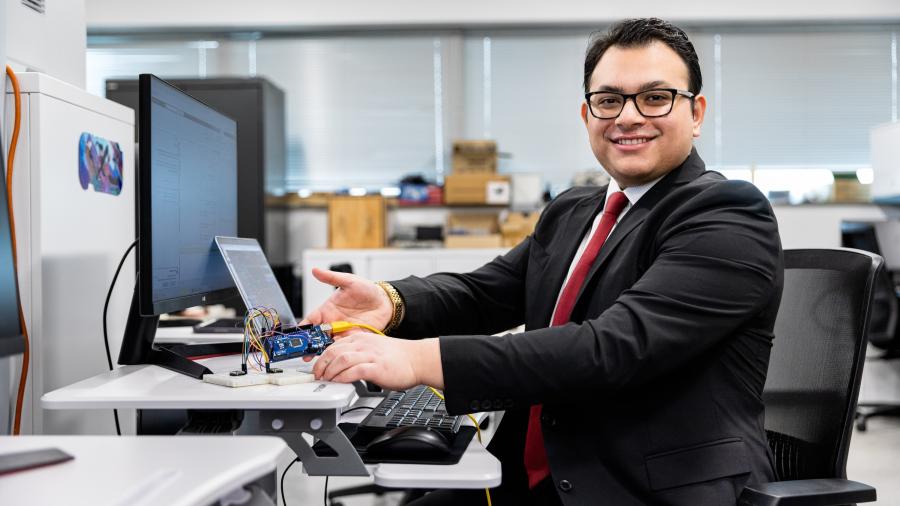 NJIT graduate Krish Poudel '26 sits at a desk, holding up a small electronic device.