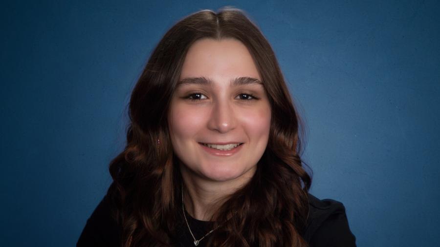 Studio portrait of NJIT graduate Kaily Peixoto '26 against a blue gradient background.