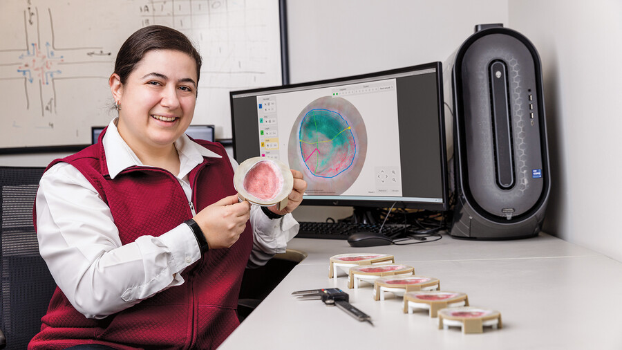 NJIT associate professor Salam Daher sits in front of a computer screen showing a digital wound model. She holds a 3D printed model of a skin anomaly.