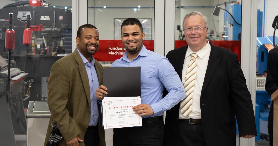 Randy Valerio, a production maintenance supervisor for a pharmaceutical company, receives his training certificate as Professor ShaQueel Dyer (left), who taught the course, and Newark College of Engineering Dean Moshe Kam (right) look on.